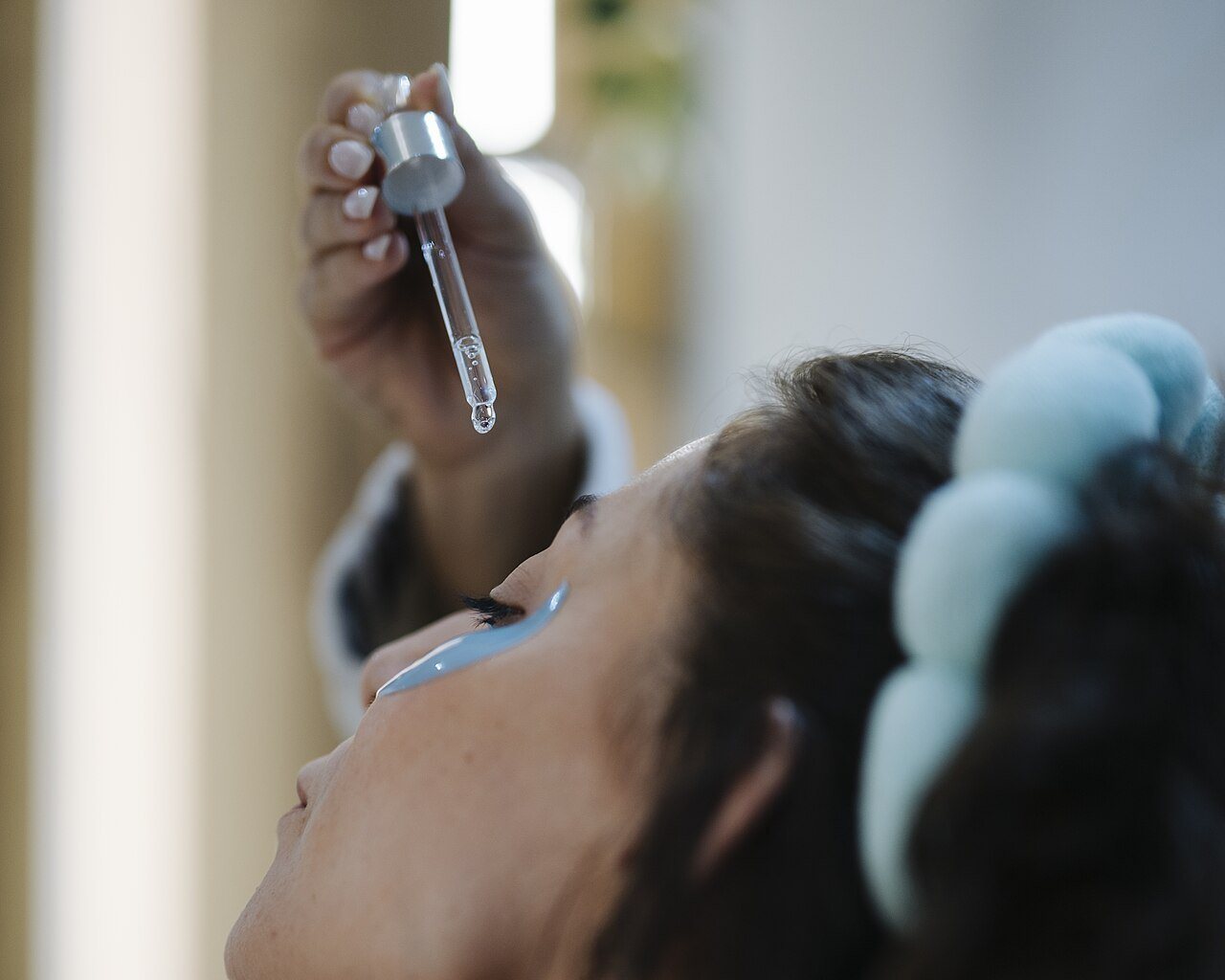 Wanita meneteskan serum wajah dengan pipet, salah satu langkah perawatan topikal untuk membantu memudarkan bekas jerawat berupa perubahan warna kulit