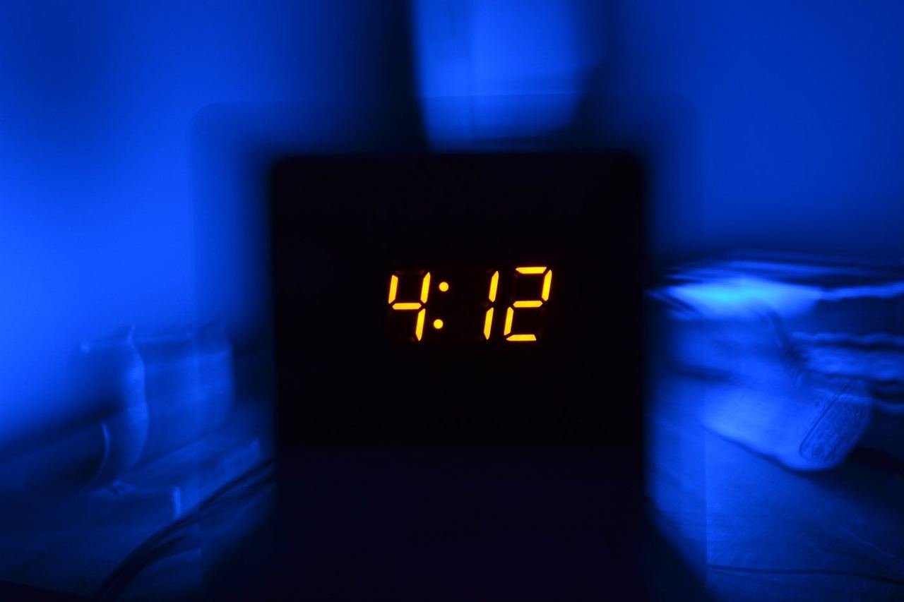 Jam alarm digital menunjukkan pukul 4:12 dini hari di kamar yang gelap, menggambarkan seseorang yang terjaga karena insomnia