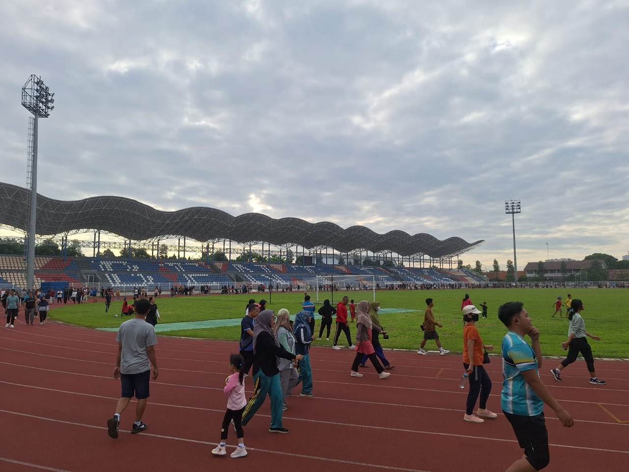 Orang-orang berjalan kaki dan berolahraga pagi hari di lintasan lari stadion, menggambarkan aktivitas fisik dan paparan sinar matahari pagi sebagai kebiasaan mendukung energi harian